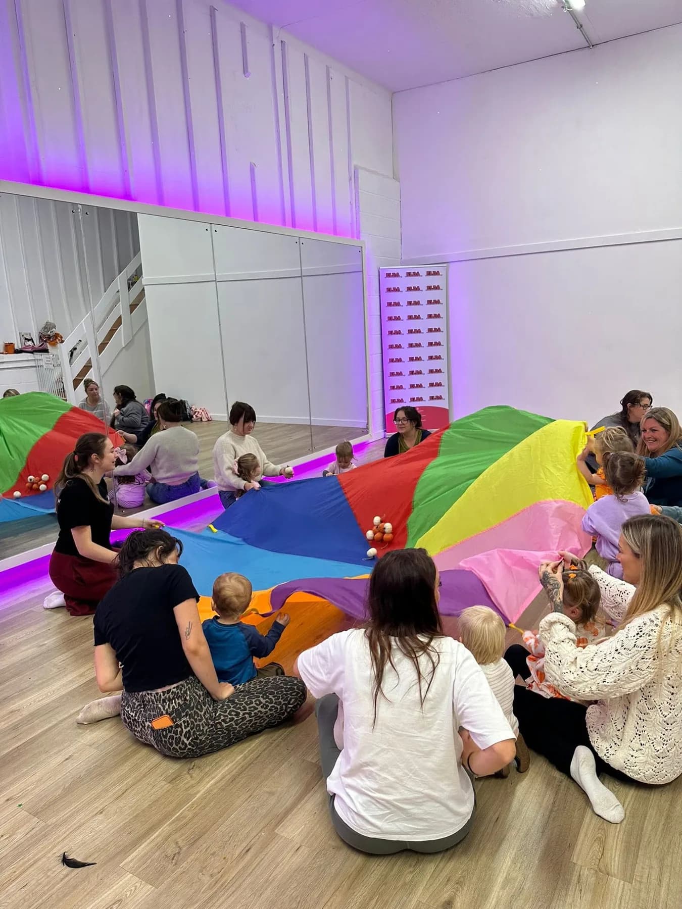 Toddlers and their grown-ups playing with a rainbow parachute in a Baby Bop class at the Camborne studio
