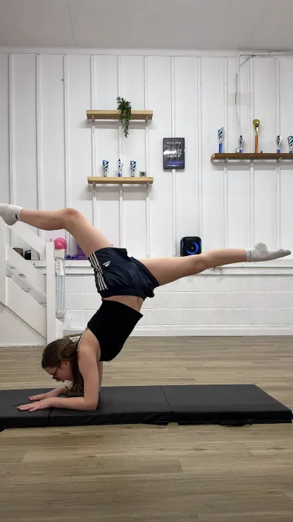 An acro dancer inverted in a controlled handstand on the mat