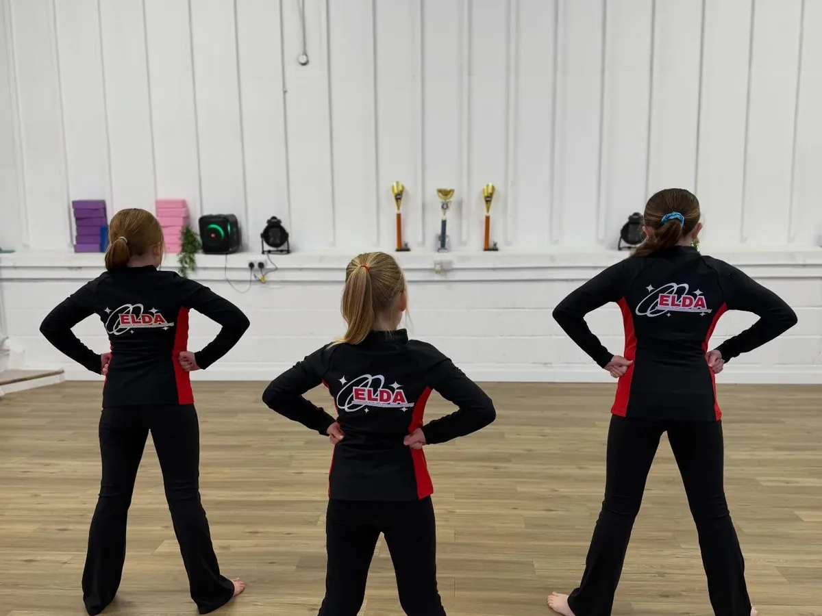 Three dancers in ELDA jackets facing the studio mirror